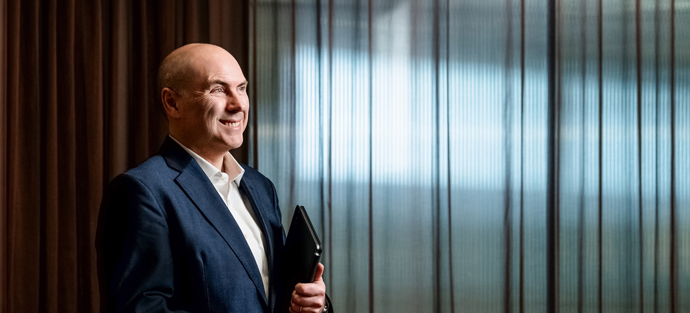 Portrait of a smiling man in a blue suit holding a folder in an office setting